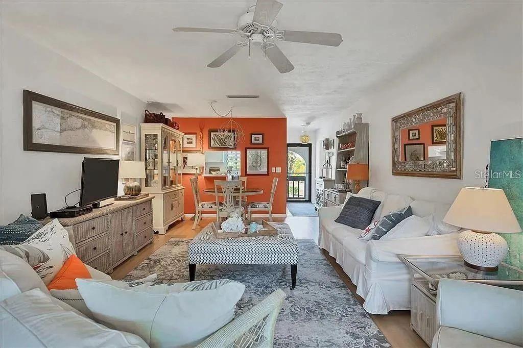 A living room and dining area feature white furniture, a patterned ottoman, and an orange wall — 1650 STICKNEY POINT ROAD UNIT 50-202, SARASOTA, FL