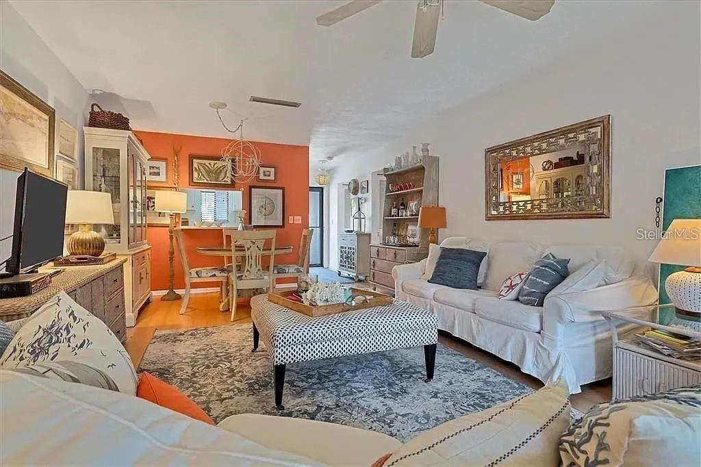 A living room and dining area feature hardwood floors, an orange accent wall, and furniture — 1650 STICKNEY POINT ROAD UNIT 50-202, SARASOTA, FL