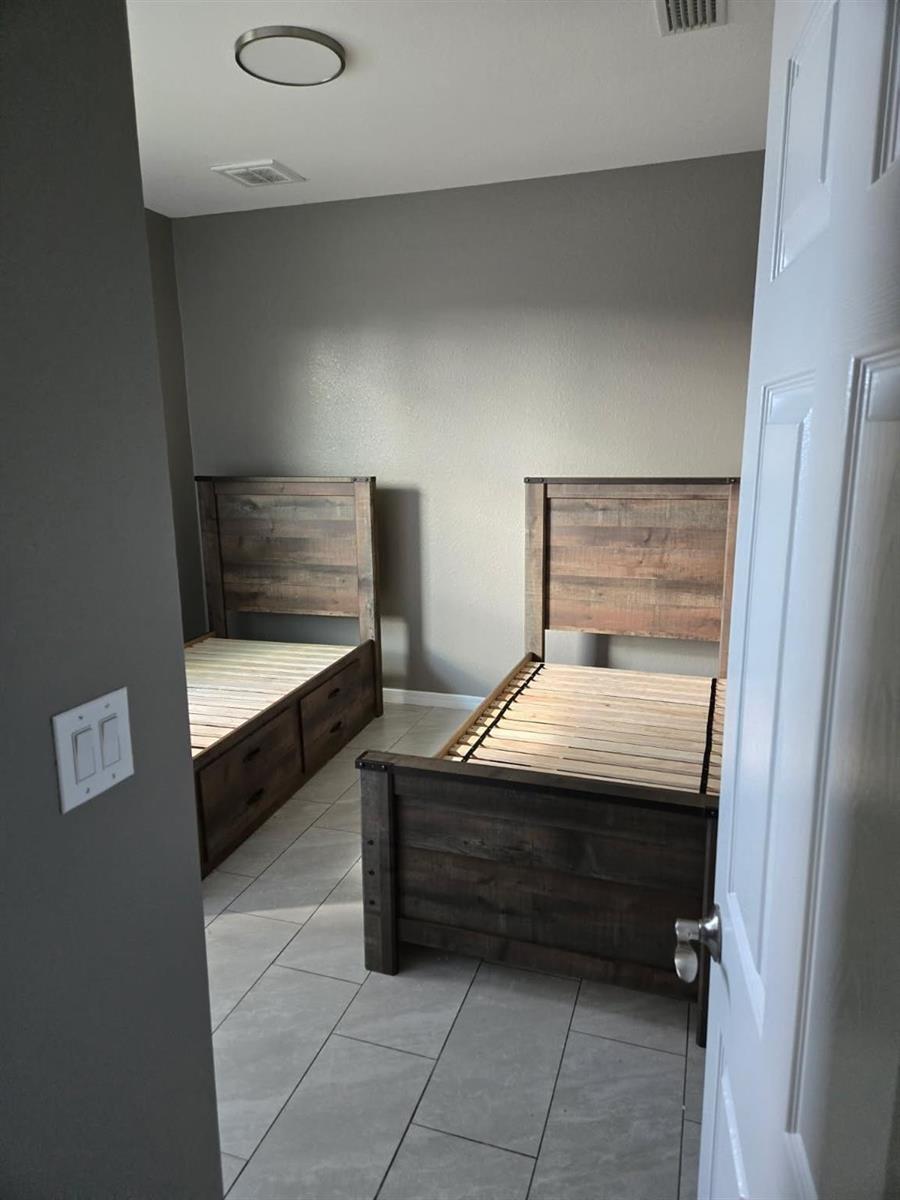 A bedroom features two rustic wooden twin beds with storage drawers on a tiled floor — 3411 18th Street, Lehigh Acres FL 33971, LEHIGH ACRES, FL