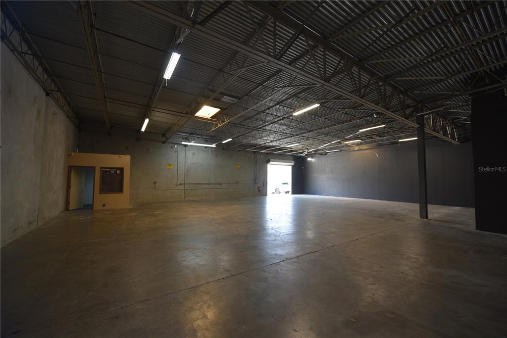 An empty industrial warehouse space features concrete floors, exposed ceiling trusses, and a roll-up door — 1211 TECH BOULEVARD UNIT 169, TAMPA, FL