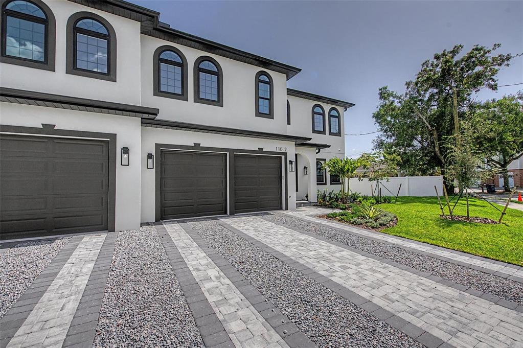 A modern two-story townhouse exterior features gray garage doors, arched windows, and a paved driveway — 110 S ARRAWANA AVENUE UNIT 2, TAMPA, FL