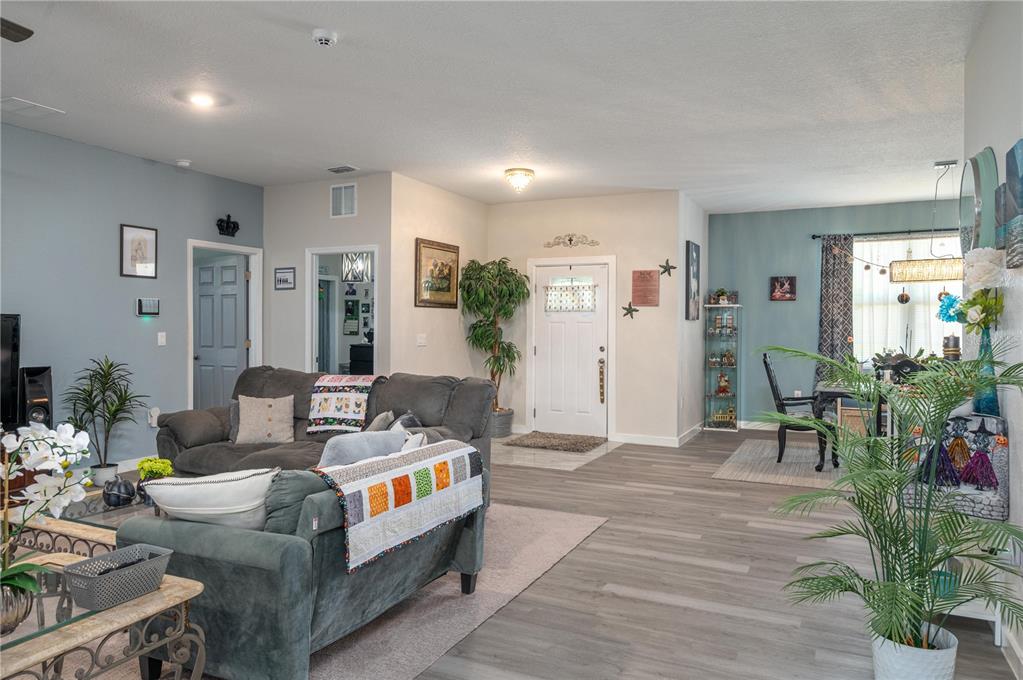 A living room and dining area feature gray wood-look flooring, light walls, and a front door — 182 WOODSTORK WAY, FROSTPROOF, FL