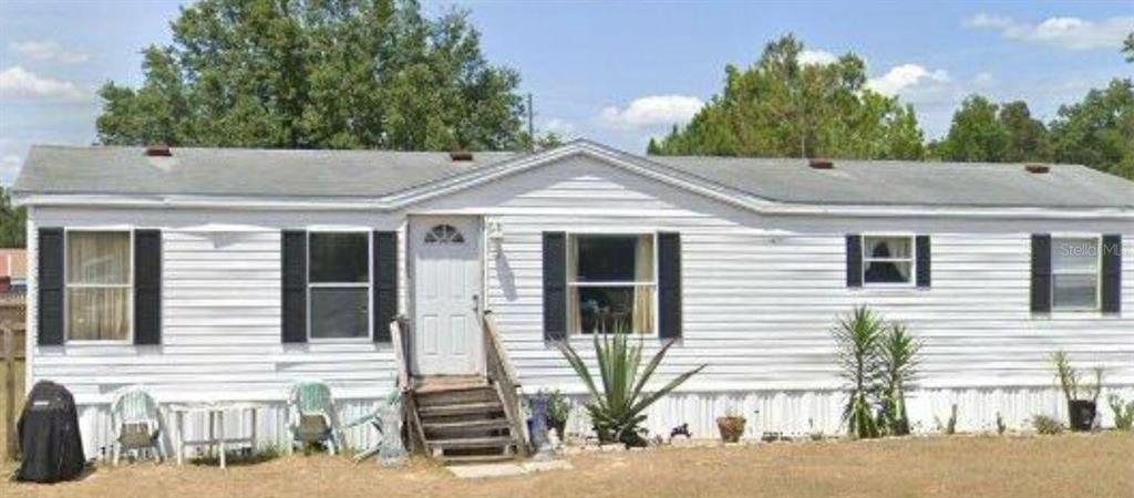 A single-story white mobile home with black shutters and a small wooden front porch — 6289 SE 140TH PLACE, SUMMERFIELD, FL
