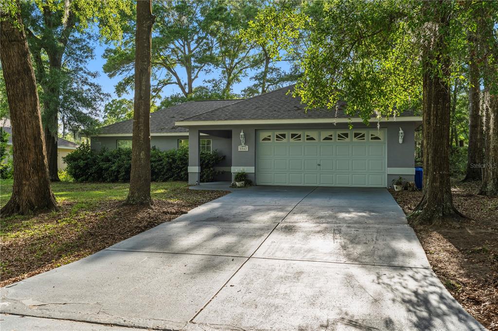A gray single-story house with a two-car garage and a concrete driveway among trees — 5542 NW 60TH TERRACE, OCALA, FL