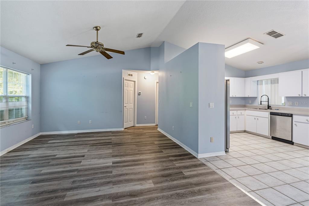 A living room with wood-look flooring transitions into a tiled kitchen with white cabinetry — 5542 NW 60TH TERRACE, OCALA, FL