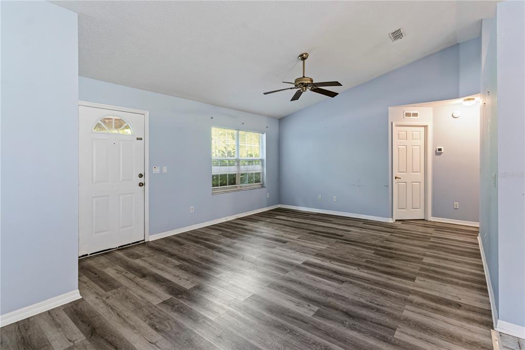 An empty living room features light blue walls, wood-look flooring, and a ceiling fan — 5542 NW 60TH TERRACE, OCALA, FL