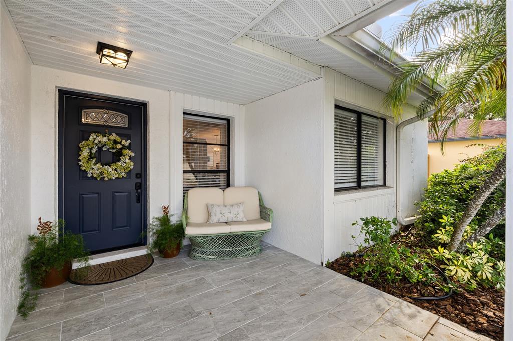 A front porch features a dark blue door, a wicker loveseat, and gray tiled flooring — 4814 FOX HUNT DR, TAMPA, FL