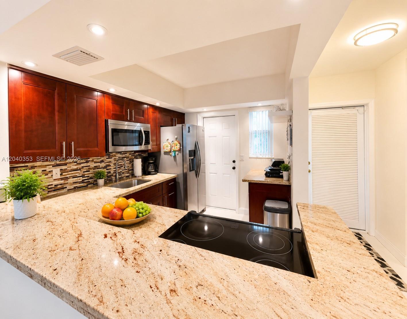 A kitchen features dark wood cabinets, granite countertops, a stainless steel refrigerator, and a cooktop — 1333 E Hallandale Beach Blvd # 106, Hallandale Beach FL 33009, HALLANDALE BEACH, FL