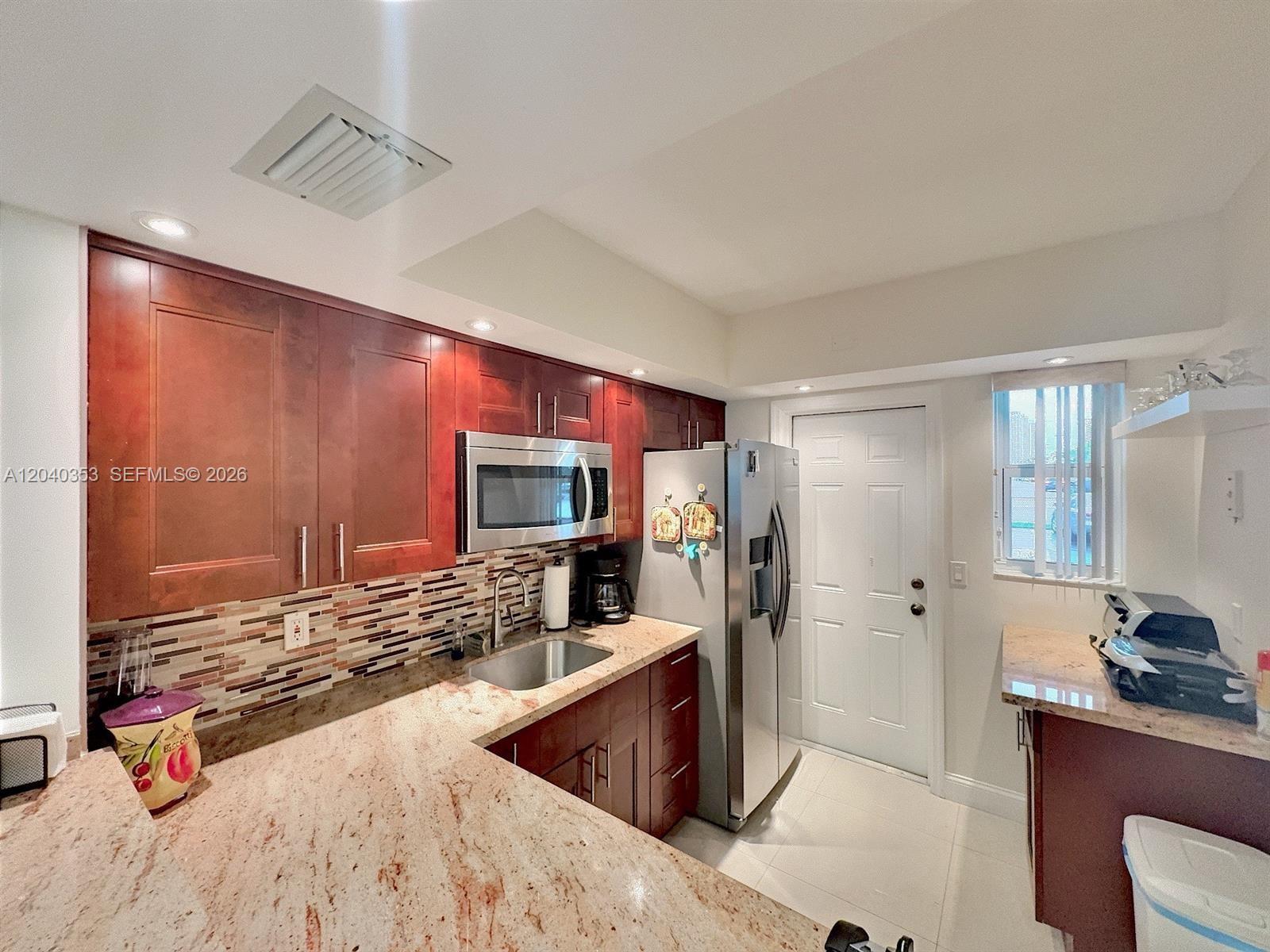 A kitchen features cherry wood cabinets, granite countertops, stainless steel appliances, and a tiled backsplash — 1333 E Hallandale Beach Blvd # 106, Hallandale Beach FL 33009, HALLANDALE BEACH, FL