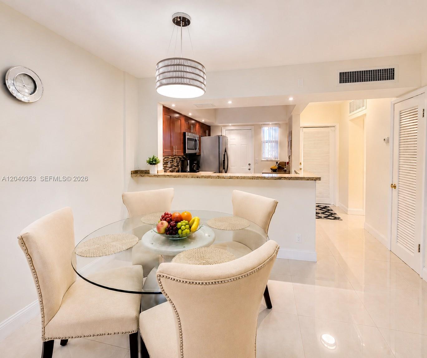 A dining area with a glass table and four chairs sits before an open kitchen — 1333 E Hallandale Beach Blvd # 106, Hallandale Beach FL 33009, HALLANDALE BEACH, FL