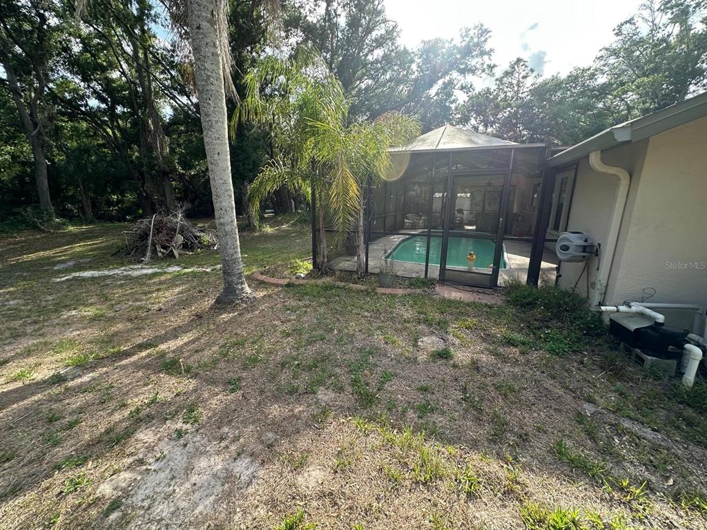 A screened-in pool sits adjacent to a house exterior with a grassy yard and trees — 3104 BROKEN ARROW COURT, WIMAUMA, FL