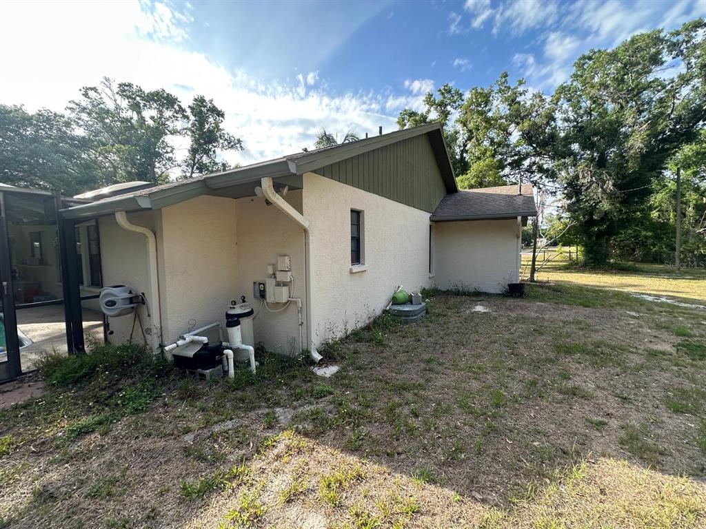 The exterior side of a house features a pool pump, stucco walls, and green siding — 3104 BROKEN ARROW COURT, WIMAUMA, FL