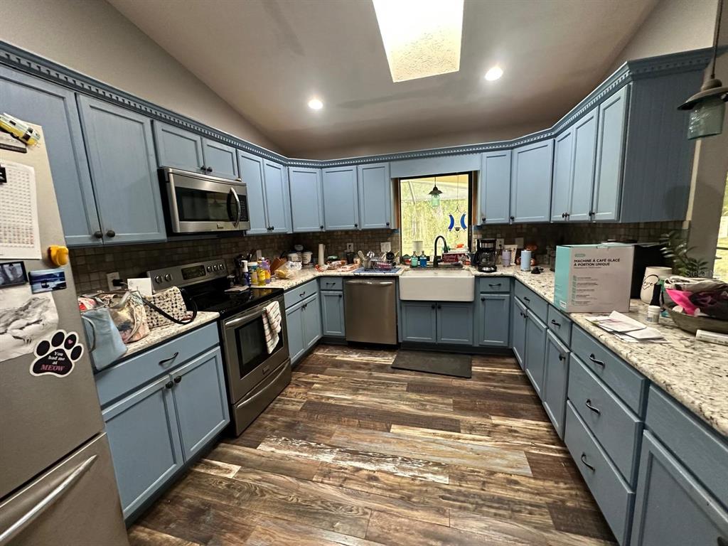 A kitchen features blue cabinets, granite countertops, stainless steel appliances, and wood-look flooring — 3104 BROKEN ARROW COURT, WIMAUMA, FL