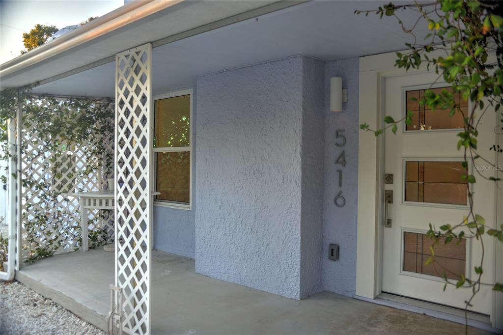 A light blue house exterior features a covered porch, a white lattice screen, and a door — 5416 4TH AVENUE W, BRADENTON, FL