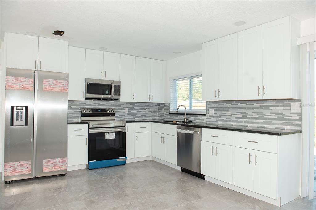 A modern kitchen features white cabinets, stainless steel appliances, and a gray tiled backsplash — 11889 93RD AVENUE, SEMINOLE, FL