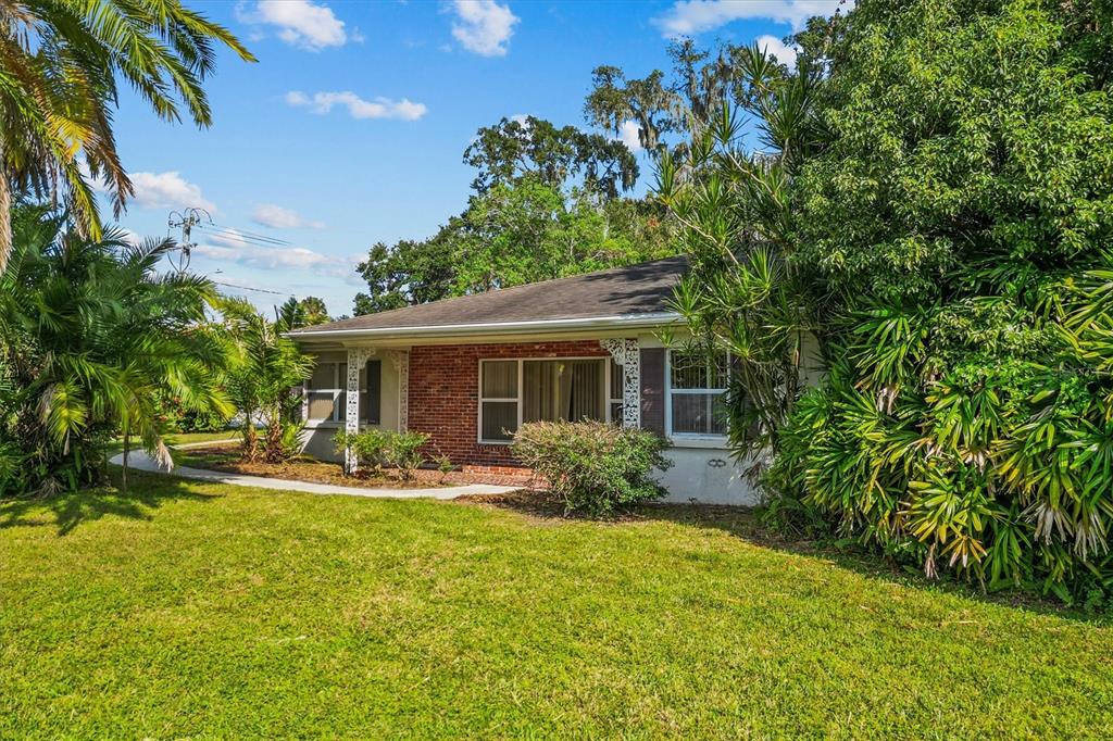 A single-story brick and stucco house sits on a grassy lot surrounded by lush landscaping — 225 LAKE HOLLINGSWORTH DRIVE, LAKELAND, FL