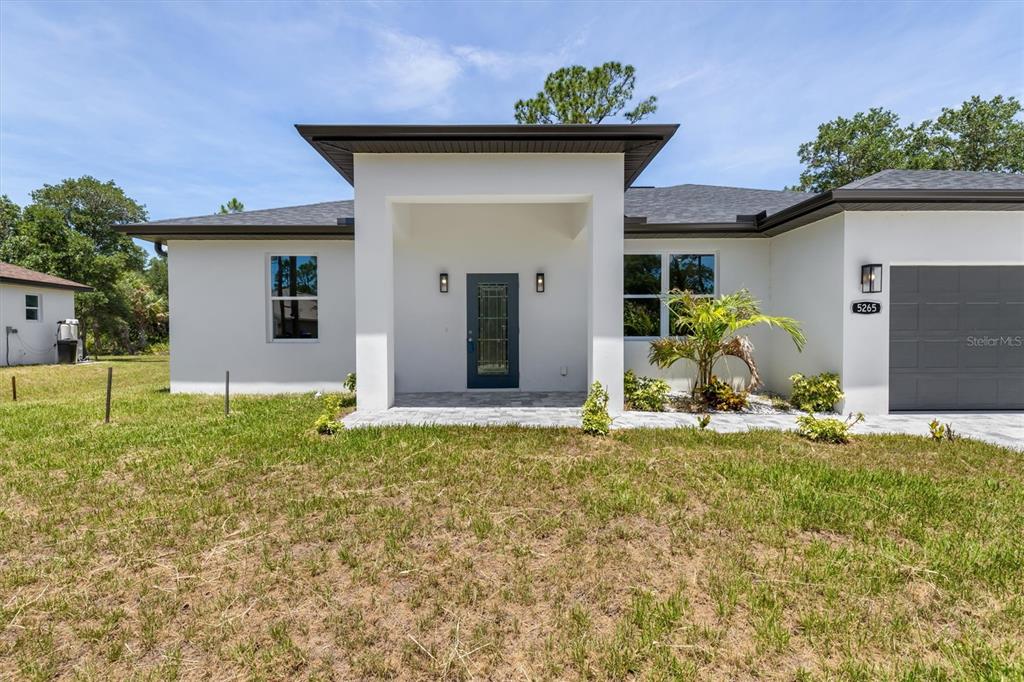 A modern, white single-story house features a dark gray garage door and a covered entryway — 5265 CAPUTO AVENUE, NORTH PORT, FL
