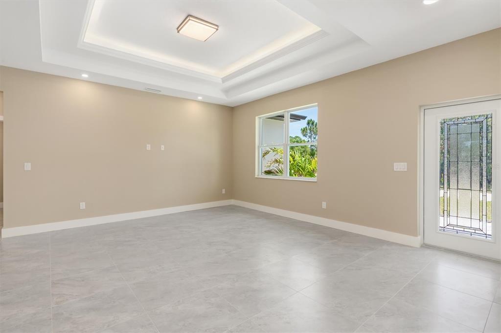 An empty room features a tray ceiling, light-colored tile flooring, and a glass-paneled exterior door — 5265 CAPUTO AVENUE, NORTH PORT, FL