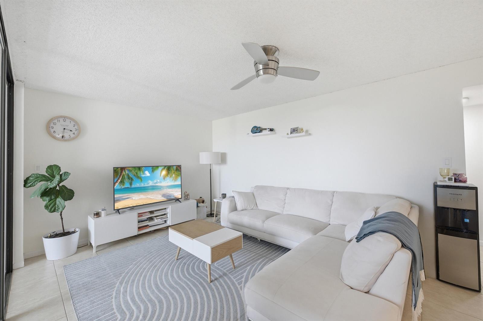 A living room features a white sectional sofa, a television on a stand, and a rug — 1915 Lavers Circle # E508, Delray Beach FL 33444, DELRAY BEACH, FL