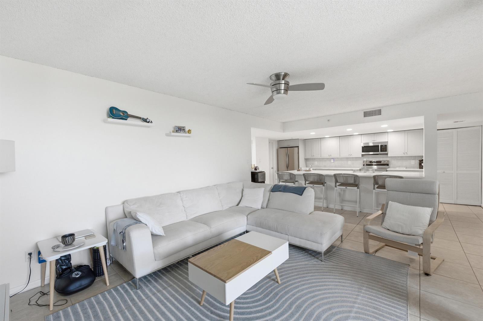 A living room with a white sectional sofa, coffee table, and an open kitchen with bar seating — 1915 Lavers Circle # E508, Delray Beach FL 33444, DELRAY BEACH, FL