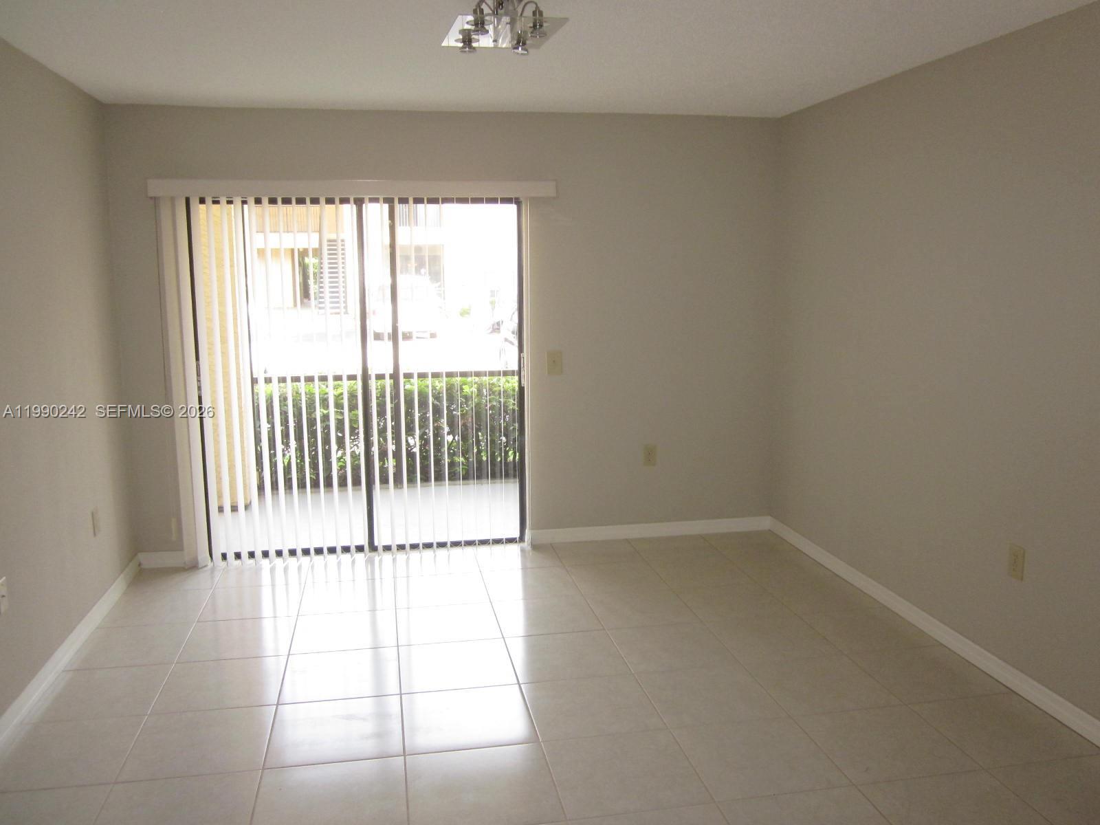 An empty room features light-colored tile flooring, neutral walls, and a sliding glass door — 15051 SW 103 LN # 4103, Miami FL 33196, MIAMI, FL