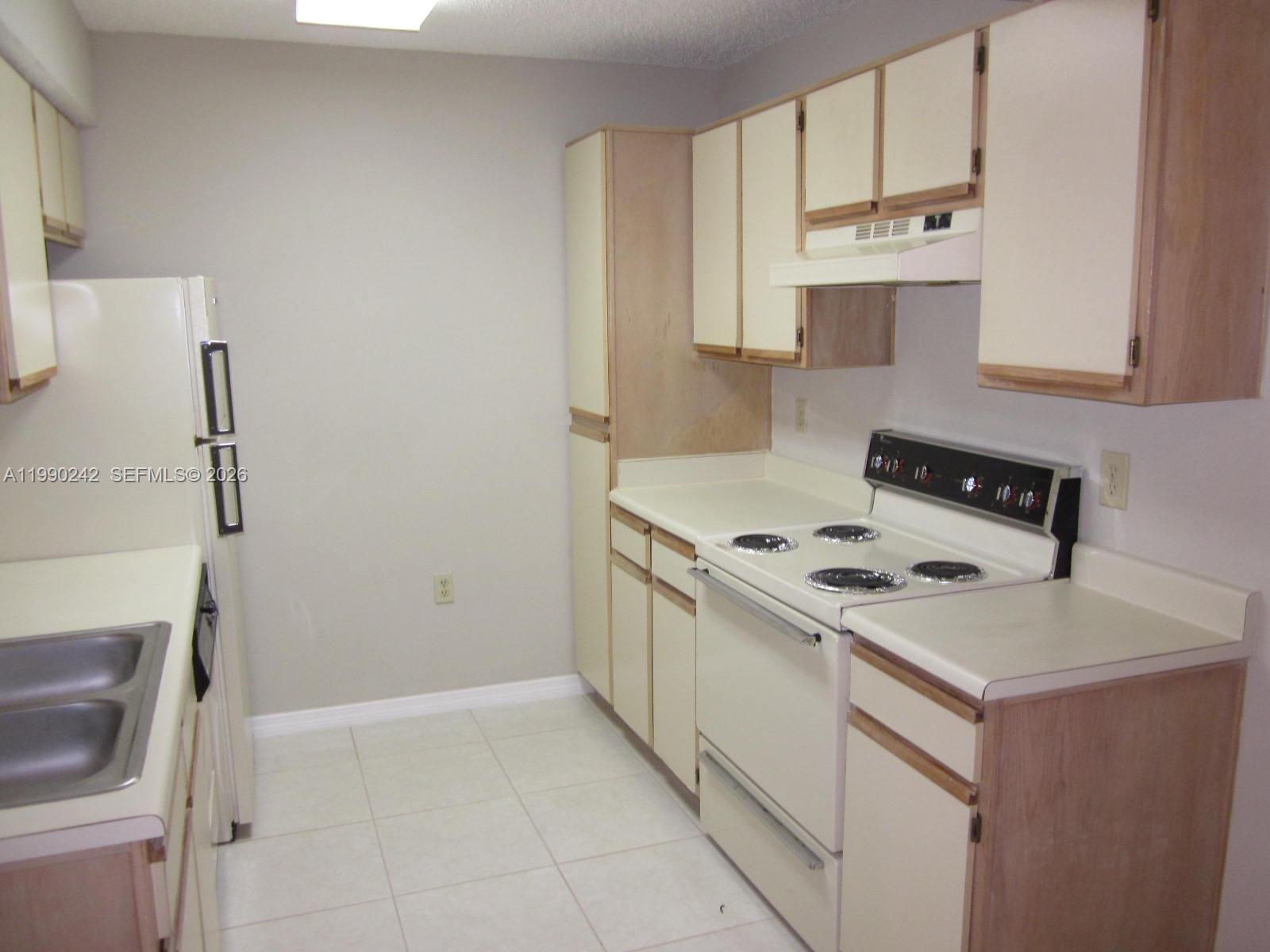 A kitchen features white appliances, light-colored cabinets, laminate countertops, and tile flooring — 15051 SW 103 LN # 4103, Miami FL 33196, MIAMI, FL
