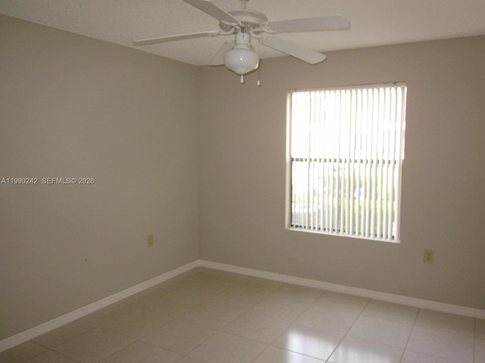 An empty room features light-colored tile flooring, beige walls, and a ceiling fan — 15051 SW 103 LN # 4103, Miami FL 33196, MIAMI, FL