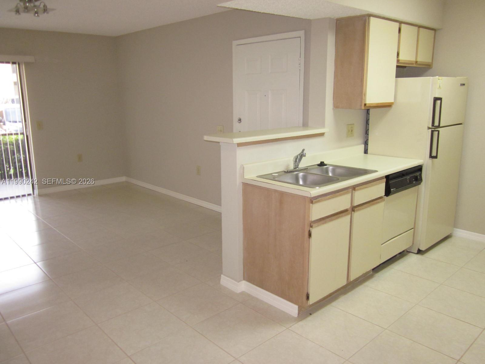 A kitchen with light-colored cabinets and a double sink overlooks an adjacent living area — 15051 SW 103 LN # 4103, Miami FL 33196, MIAMI, FL