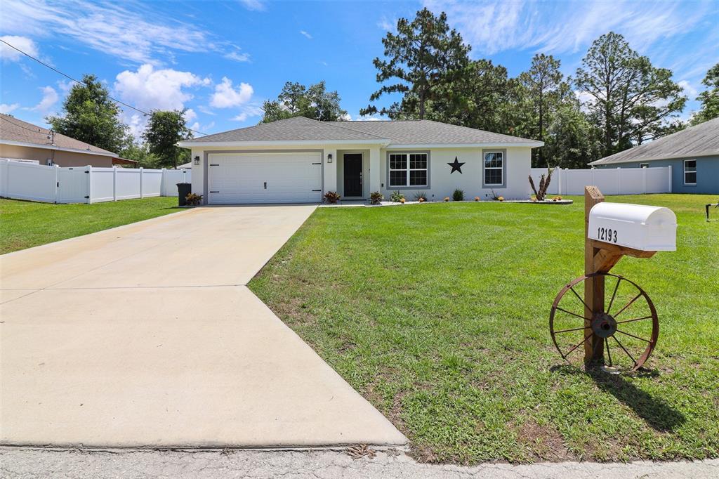 A single-story house with a white exterior, a two-car garage, and a decorative wagon wheel mailbox — 12193 SE 87TH TERRACE, BELLEVIEW, FL