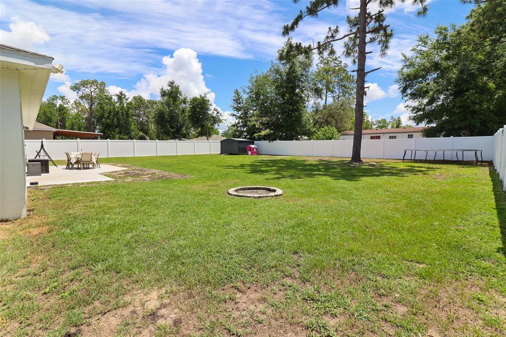 A spacious backyard features a grassy lawn, a concrete patio, and a white privacy fence — 12193 SE 87TH TERRACE, BELLEVIEW, FL
