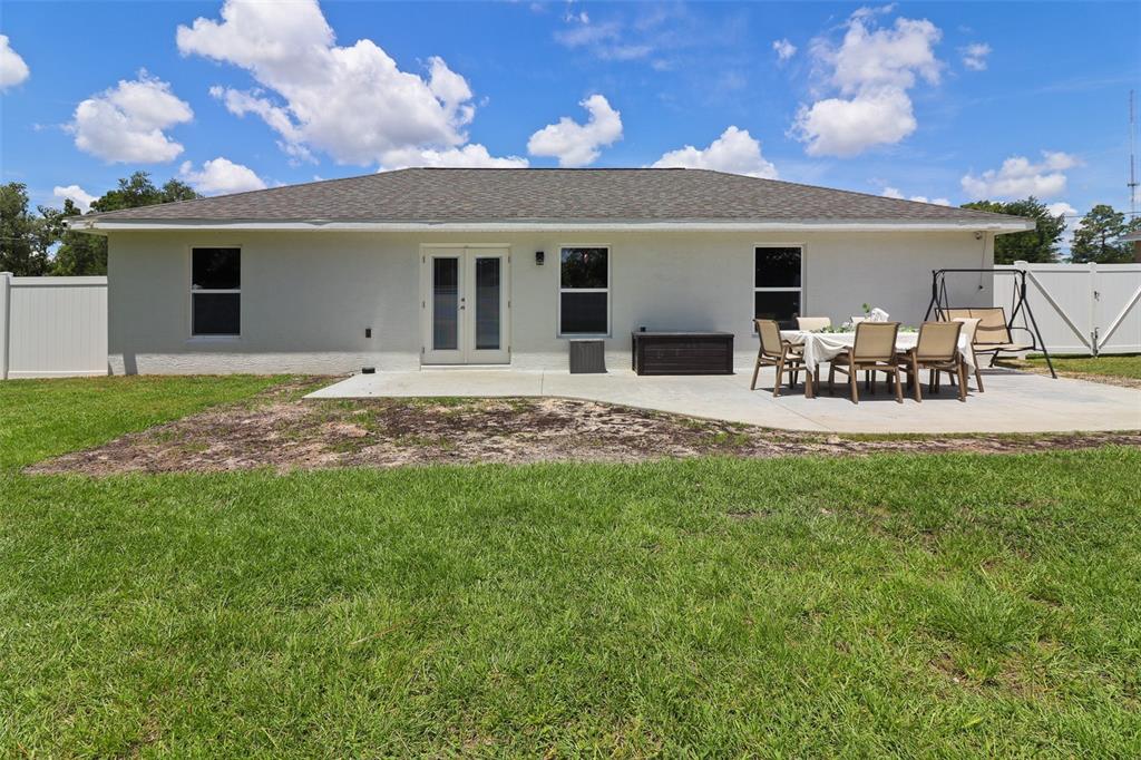 The back exterior of a single-story house features a concrete patio and a grassy yard — 12193 SE 87TH TERRACE, BELLEVIEW, FL
