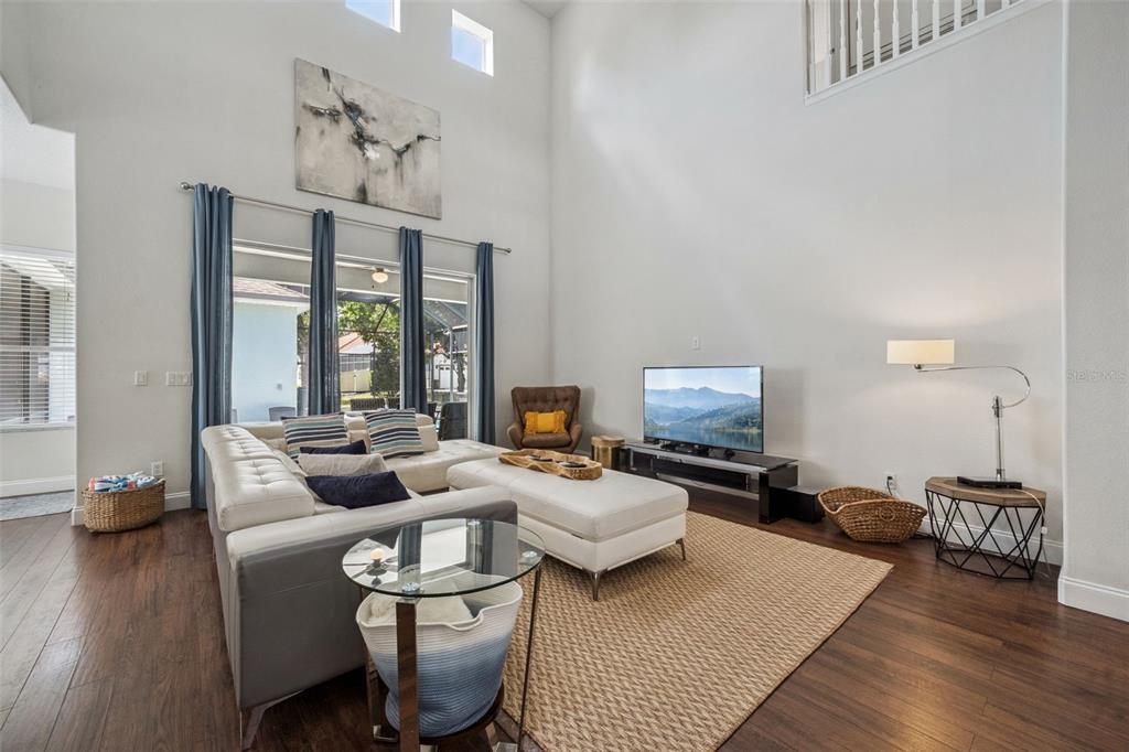 A living room features high ceilings, a white sectional sofa, and dark wood flooring — 7412 DEVEREAUX STREET, KISSIMMEE, FL