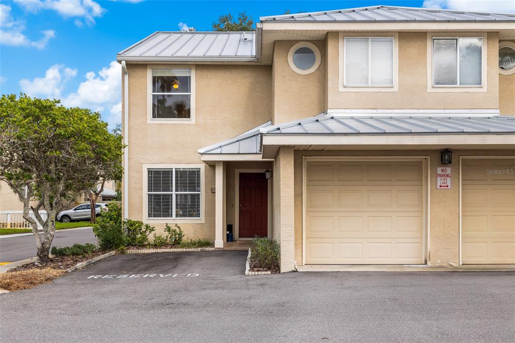 A two-story tan townhouse with a metal roof, a single-car garage, and a reserved parking space — 13007 LORNA PLACE, TAMPA, FL