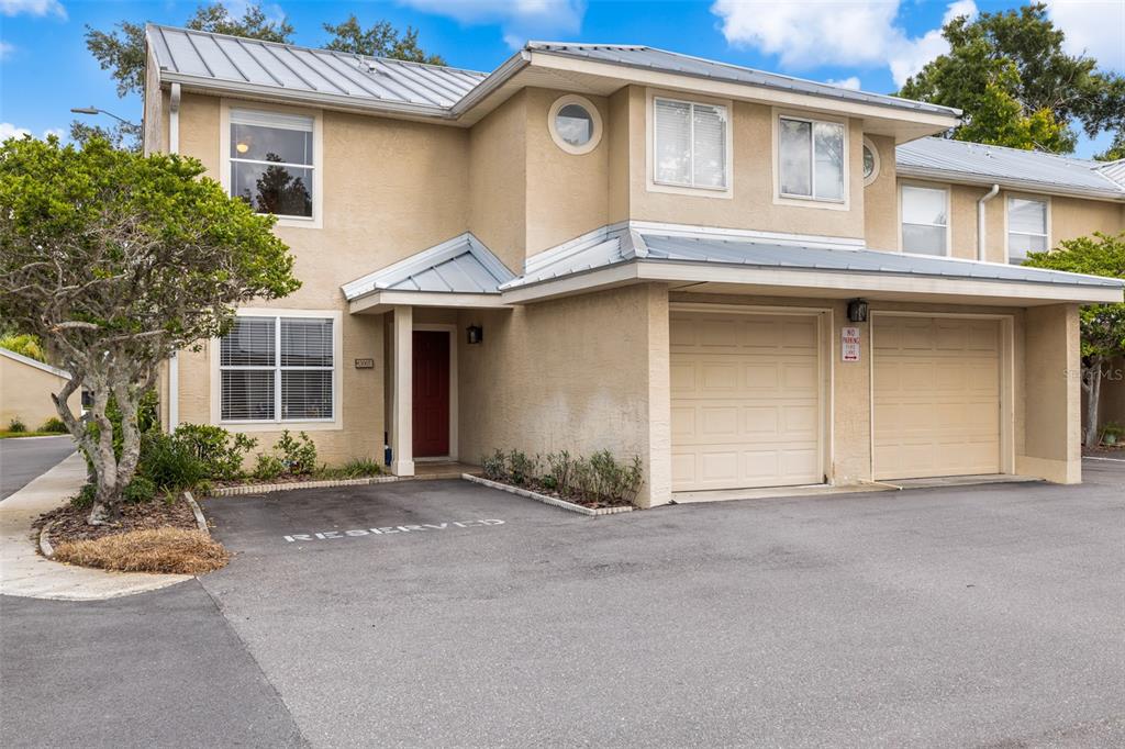 A two-story tan stucco townhouse features a metal roof, two garage doors, and a reserved parking space — 13007 LORNA PLACE, TAMPA, FL