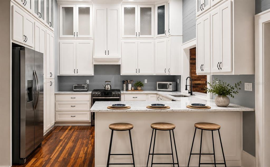 A kitchen features white cabinetry, granite countertops, a breakfast bar with stools, and hardwood floors — 18406 HIGH SPRINGS MAIN STREET, HIGH SPRINGS, FL