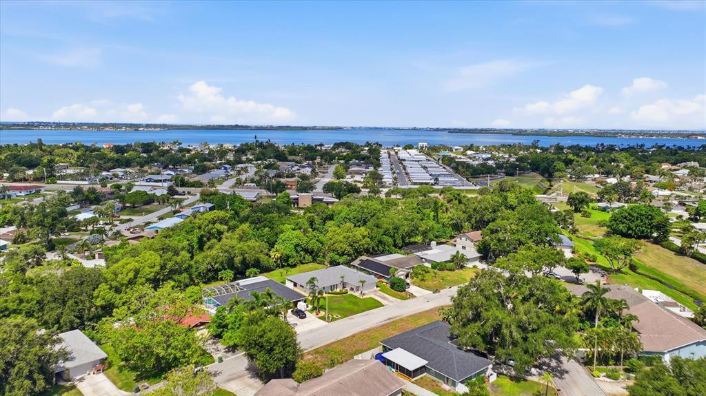 An aerial view shows a suburban neighborhood with houses, lush trees, and a distant bay — 2130 72ND STREET CIRCLE W, BRADENTON, FL