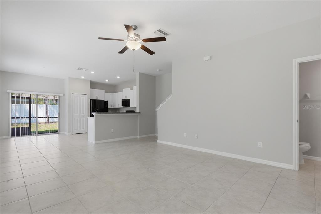 An open-concept living area features light tile flooring, a kitchen with white cabinets, and sliding doors — 4540 GLOBE THISTLE DRIVE, TAMPA, FL