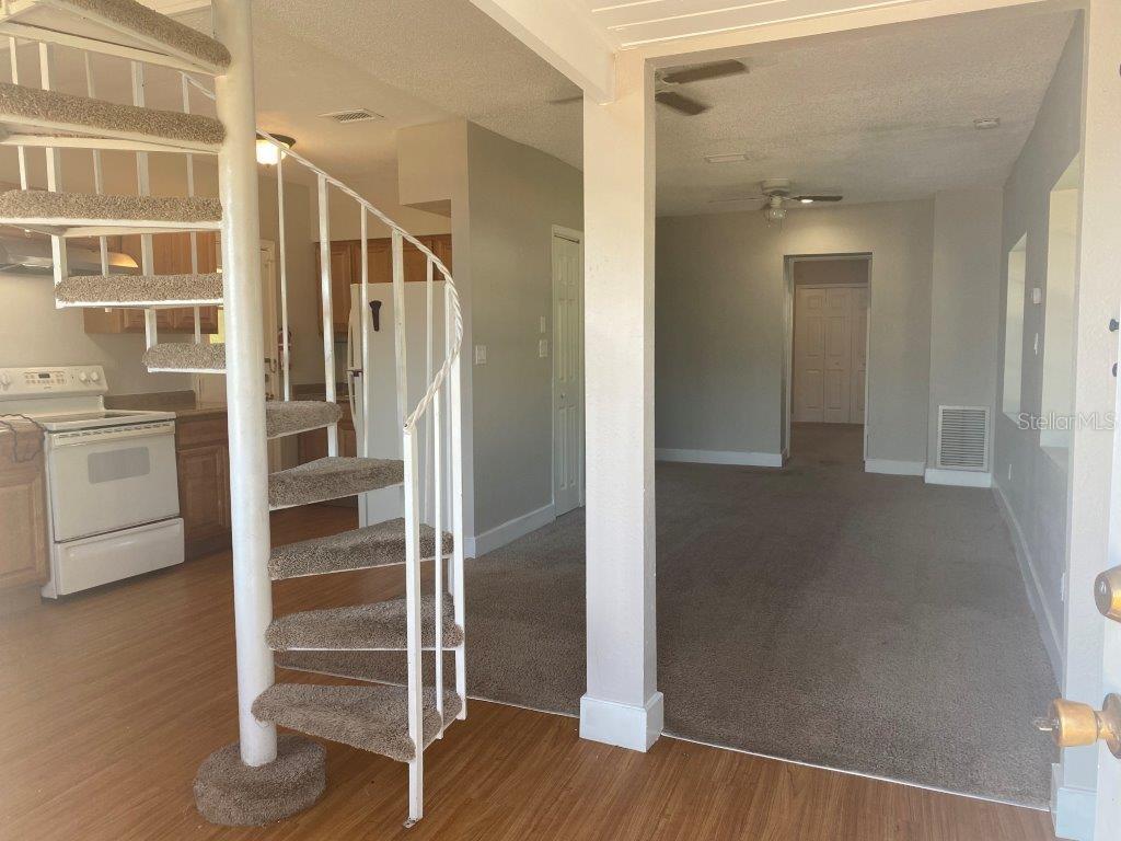 A spiral staircase stands in a room with wood-look flooring next to a carpeted living area — 741 W OSCEOLA STREET, CLERMONT, FL