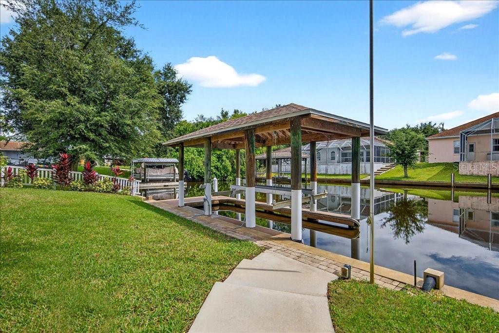 A covered boat dock sits on a canal next to a grassy lawn and house — 83 COVINGTON LANE, PALM COAST, FL