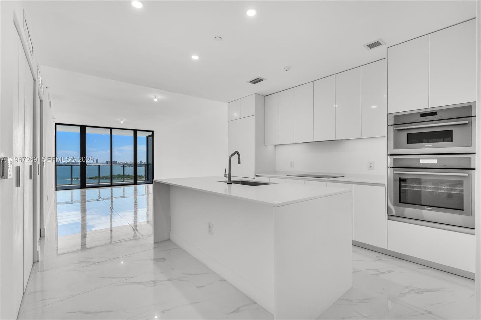 A modern white kitchen features a central island, stainless steel appliances, and floor-to-ceiling windows — 700 NE 24th ST # 1806, Miami FL 33137, MIAMI, FL