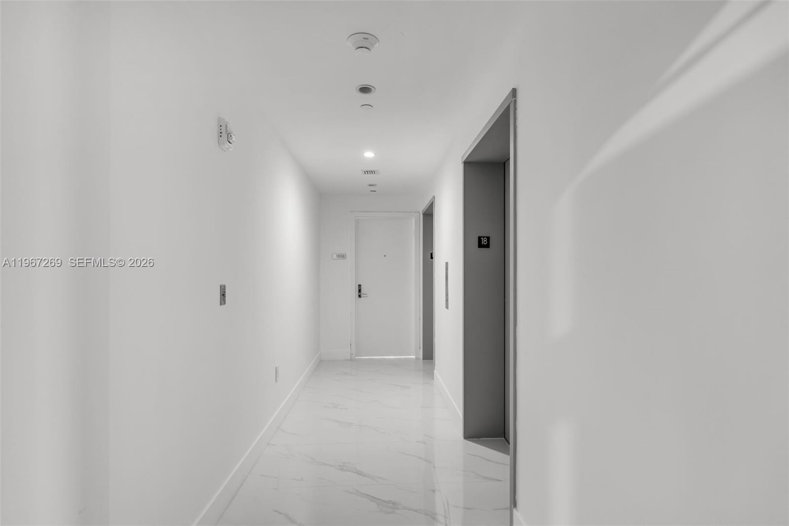 A bright, minimalist hallway features white walls, marble-style flooring, and an elevator entrance — 700 NE 24th ST # 1806, Miami FL 33137, MIAMI, FL