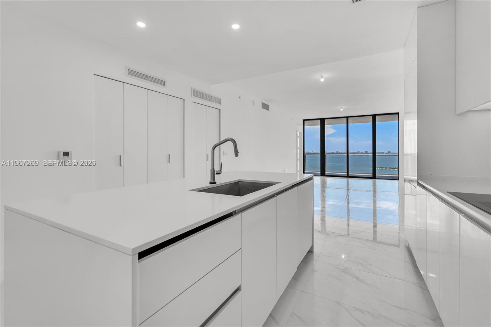 A modern white kitchen features a central island with a sink and water views — 700 NE 24th ST # 1806, Miami FL 33137, MIAMI, FL