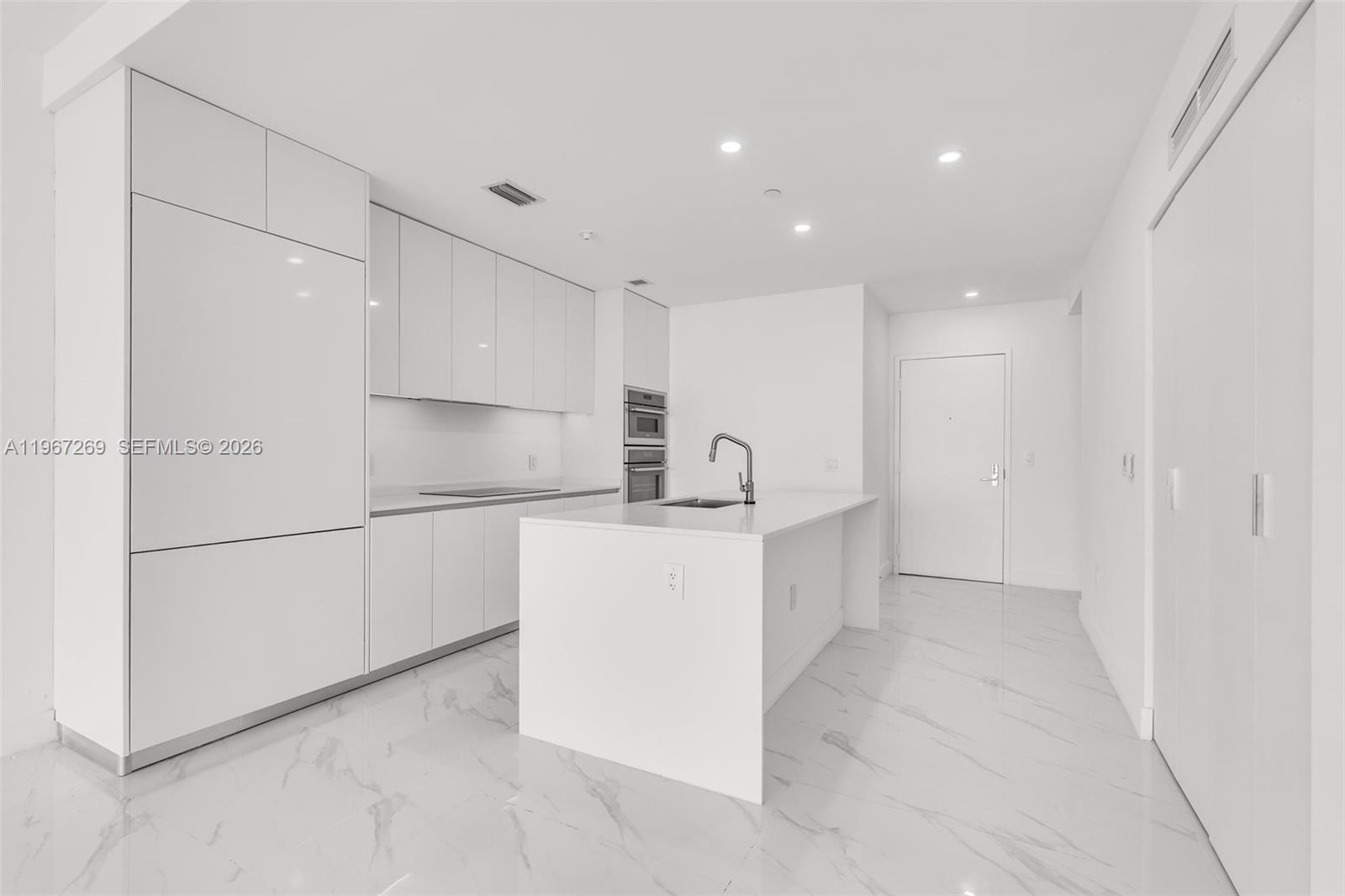 A modern white kitchen features an island, integrated appliances, and marble-patterned tile flooring — 700 NE 24th ST # 1806, Miami FL 33137, MIAMI, FL