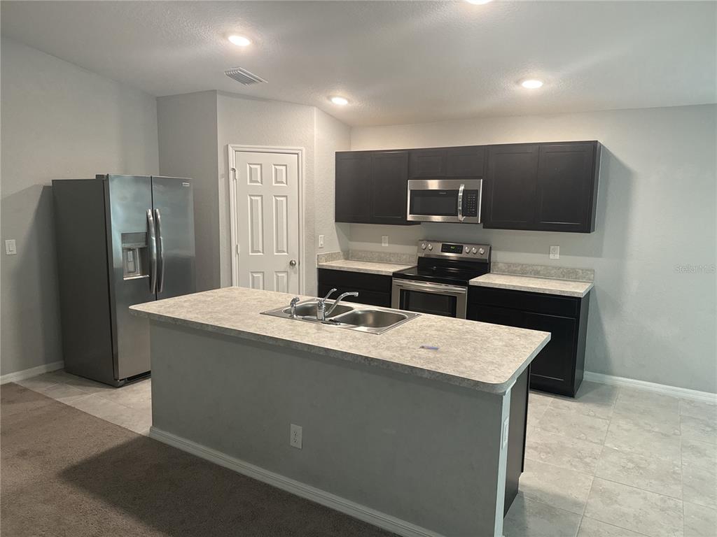 A kitchen features dark cabinets, stainless steel appliances, a central island, and light-colored countertops — 154 AUSTRALIAN DRIVE, ROTONDA WEST, FL