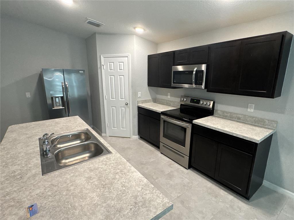 A kitchen features dark cabinets, stainless steel appliances, and a large island with a sink — 154 AUSTRALIAN DRIVE, ROTONDA WEST, FL