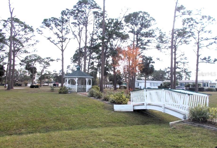 A white wooden footbridge leads to a gazebo in a grassy park with tall trees — 5420 HOLIDAY PARK BOULEVARD, NORTH PORT, FL