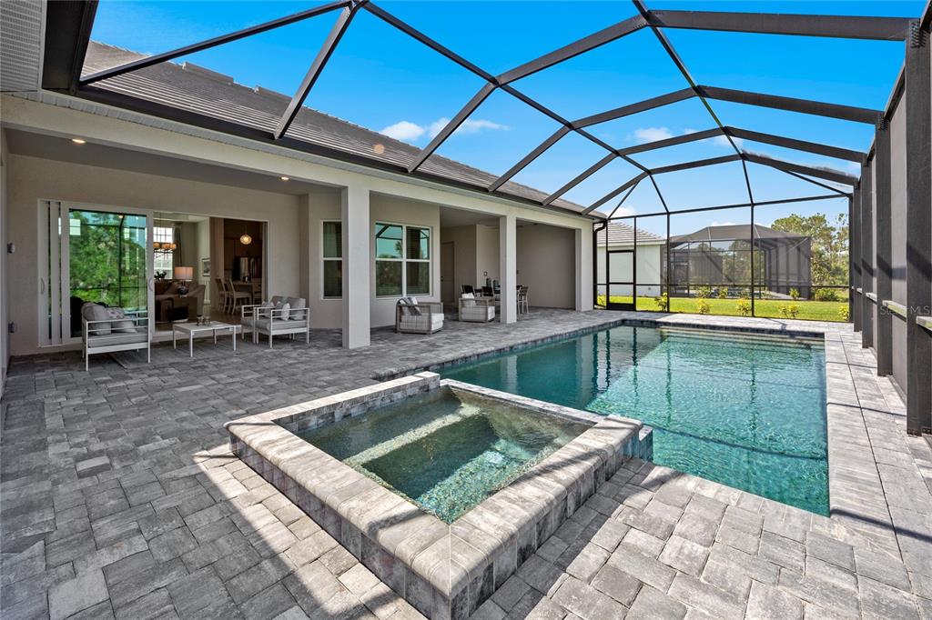 A covered patio features a pool and spa with stone pavers and a screen enclosure — 18923 CHERRYSTONE WAY, LAKEWOOD RANCH, FL