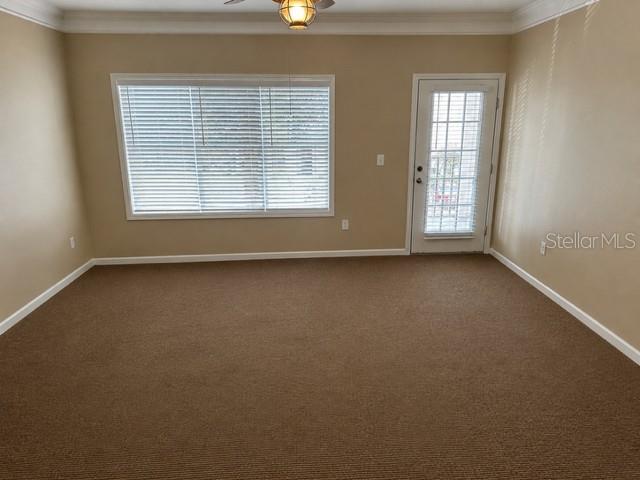 An empty room with beige walls, brown carpeting, a large window with blinds, and a door — 4802 51ST STREET W UNIT 1805, BRADENTON, FL