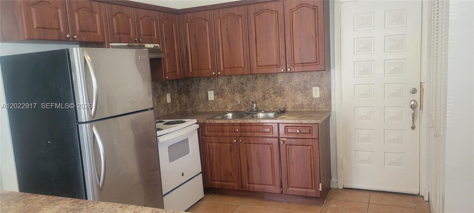 A kitchen features wood cabinets, a stainless steel refrigerator, a white stove, and tile flooring — 71 NW 18th Ave, Miami FL 33125, MIAMI, FL