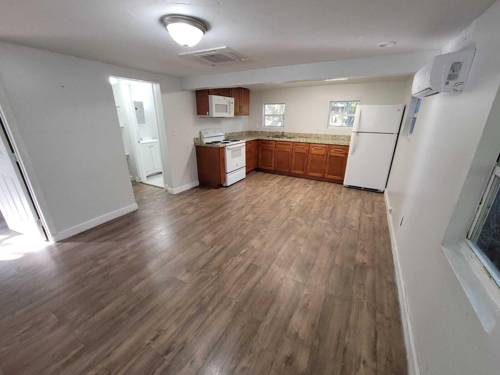 An open-concept kitchen features wood cabinets, granite countertops, white appliances, and wood-look flooring — 210 SW 7th Street, Dania Beach FL 33004, DANIA BEACH, FL